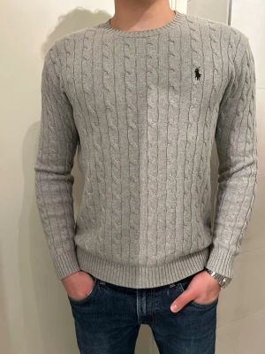 Grå Kabelstickad Ralph Lauren  - En riktigt snygg grå kabelstickad tröja från Ralph Lauren. Tröjan har en lätt slim fit from så den följer kroppen snyggt. Väl omhändertagen. Storleken är S och modellen är 176cm. Tveka inte med att ställa frågor! Priset kan diskuteras!