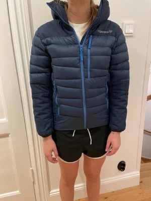 Mörkblå dunjacka från Norrøna - Snygg mörkblå dunjacka från Norrøna med huva och dragkedjor i blått. Jackan har två sidofickor med dragkedja och en bröstficka. Quiltad design som håller värmen och ger en sportig look. Perfekt för kalla dagar. Hör av er om ni har några frågor eller tydligare bilder🤗