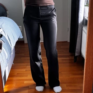 Svarta kostymbyxor från Nelly - Svarta kostymbyxor från Nelly med raka ben och klassisk passform. Byxorna har hällor för bälte, två fickor fram och två dekorativa fickor bak. Snyggt skräddad look i ett mjukt material som känns bekvämt hela dagen. Sömmarna har gått upp lite lägst ner vid benen 