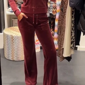 Vinröda velourbyxor Juicy Couture XS - Vinröda mjukisbyxor från Juicy Couture i velour med bred resår i midjan. Byxorna har raka ben, stora fickor framtill och klassisk logga broderad på ena fickan. Perfekta för en chill och trendig look. Snörena saknas och ett märke på låret! Annars fint skick! Nypris 1200kr