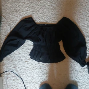 Svart blus med puffärmar från Gina Tricot - Supersnygg svart blus från Gina Tricot med markerad midja och stora puffärmar. Blusen har en fyrkantig urringning och är tillverkad i ett lätt, transparent tyg som ger en cool och trendig look.