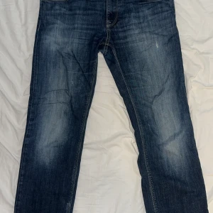 Hugo boss jeans - Snygga mörkblå jeans från Hugo boss med klassisk rak passform och diskreta slitningar framtill. Jeansen har fem fickor, kontrastsömmar och är tillverkade i robust denim. Perfekta för dig som gillar en tidlös och avslappnad stil.