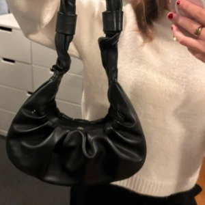 Svart axelväska från Pieces i skinnimitation - Säljer en svart axelväska från Pieces i skinnimitation. Väskan har en cool, rynkad design och ett rejält handtag med knutdetaljer. Perfekt storlek för det viktigaste och stängs med magnetknapp. Enkel att matcha till olika outfits.