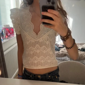 Vit spetsblus från Zara med puffärm - Superfin vit blus från Zara med broderade spetsdetaljer och stickad struktur. Puffiga korta ärmar, v-ringad halsringning med broderad kant och volang. Perfekt till jeans eller kjol för en söt och trendig look.