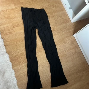 Svarta vida byxor i crinkle-tyg - Svarta byxor med hög midja och vida ben i ett snyggt crinkle-material. De har en elastisk midja och är riktigt sköna och lätta att bära. Perfekta om du gillar en avslappnad men trendig look.