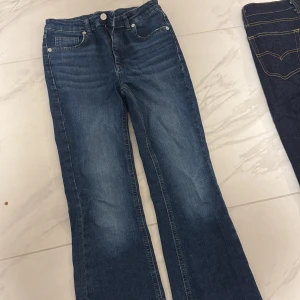 Blå bootcut jeans från RYVLS - Säljer mina RYVLS jeans för dem har blivit för små! Snygga low rise blå jeans med bootcut passform och klassisk femficksdesign. Jeansen har en lätt tvättad look med slitningar på låren och raka ben som blir vidare nedtill. Tillverkade i mjukt denimtyg med dragkedjegylf och silverfärgade nitar.