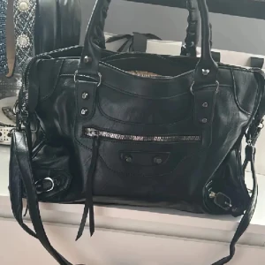 Balenciaga city liknande väska  - Påminner om balenciaga city bagen, aldrig använd. Köpt på en marknad i Spanien, men har somsagt tyvärr inte blivit använd. Passar till skolan/jobba då de får plats en del, ex dator, böcker osv. Måtten är:  12 cm djup (botten på väskan), 37 cm bred, 22 cm hög Skriv om du undrar något!🩷