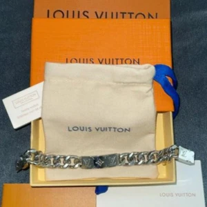 Louis Vuitton silverfärgat armband - Stilrent armband från Louis Vuitton i blankt silverfärgat metall med kraftig kedja och graverad LV-logga på plattan. Kommer med original ask och dustbag. Perfekt accessoar för dig som vill ha en lyxig och trendig detalj till din outfit.