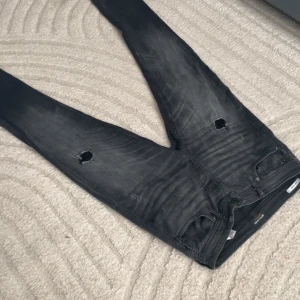 Svarta skinny jeans Jack & Jones 32/34 - Svarta skinny jeans från Jack & Jones i modellen Glenn. Jeansen har slitna detaljer med hål på båda knäna och en snygg tvättad look. Klassisk femficksmodell och smal passform som sitter tajt hela vägen ner.