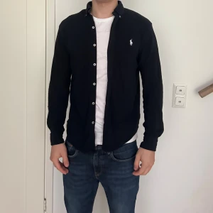 Svart skjorta från Ralph Lauren - Mörkblå långärmad skjorta från Ralph Lauren med klassisk button-down krage och vit broderad logga på bröstet. Storlek S men passar också till storlek M. Mycket bra skick. Om du har mer fårgor., skicka gärma ett meddelande till mig!