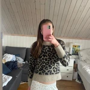 Leopardmönstrad stickad tröja Stories - Säljer en supermjuk stickad tröja från & Other Stories i beige med svart leopardmönster. Tröjan har bred ribbad mudd vid hals, ärmslut och nederkant. Perfekt för dig som vill sticka ut med ett djurmönster i höst och vinter.