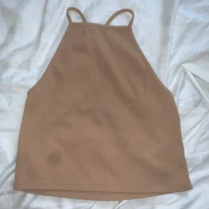 Beige ribbad topp - Säljer en beige ribbad topp från Bik Bok i storlek M. Toppen har smala axelband som korsas i ryggen och en hög halsringning. Materialet är mjukt och stretchigt, perfekt för en enkel och clean look.