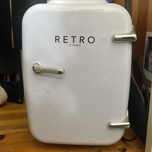 Bredeco Retro Mini Kylskåp - Snyggt retro-inspirerat mini kylskåp från Bredeco i vitt. Perfekt för kontor, sovrum eller resor. Inredningen är fräsch och ren, med mindre ytliga märken på utsidan. Kompakt design med kromade handtag och dörrfack för extra förvaring.