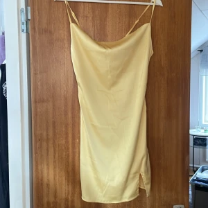 Gul satinklänning - Säljer en elegant gulfärgad  slipklänning med tunna axelband och mjuk, glansig satinfinish. Den har klister som ej har försvunnit men antar att det går bort i tvätten (finns på insidan av bröstet)