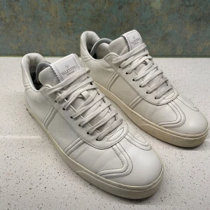 Valentino flycrews - Snygga vita sneakers från Valentino Garavani i läder med stilrena sömdetaljer och klassisk snörning. Perfekta för dig som gillar exklusiva och minimalistiska sneakers. Storlek 43 men sitter mer som 43,5  44. Alla nitar är kvar och om du har några funderingar så är det bara att höra av sig😁