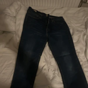 Mörkblå jeans med klassisk passform - Säljer ett par mörkblå jeans med klassisk femficksdesign och lätt slitning på låren. Jeansen har rak passform och normal midja, perfekta till en avslappnad stil. Materialet är robust denim som håller länge.