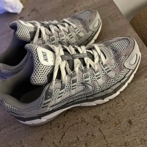 Nike p6000 grå mesh sneakers - Nike sneakers i grått och silver med meshpaneler och detaljer i syntet och mocka. Skorna har snörning, vit sula och klassisk Swoosh-logga på sidan. Perfekta för dig som gillar sportig och clean stil.