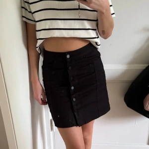 Svart jeanskjol med knappar - Snygg svart kort jeanskjol från Gina. 