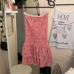 Rosa mönstrad kortklänning Gina Tricot - Supersöt kortklänning från Gina Tricot i rosa och ljusgult mönster. Klänningen har smockad överdel, volangig kjol och tunna axelband. Perfekt för varma dagar och ger en riktigt somrig vibe!