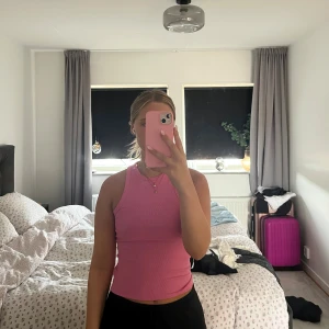 Rosa ribbad linnetopp - Säljer en rosa ribbad linnetopp med tight passform och ärmlös design. Toppen har en hög halsringning och är perfekt för dig som gillar en enkel men snygg stil. Passar till både jeans och kjol för en trendig look.