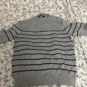 Grå randig tröja från 157 XS - Grå tröja från 157 i storlek XS med svarta horisontella ränder. Tröjan har ribbade muddar vid hals, ärmslut och nederkant. Klassisk och enkel design som funkar året runt. Materialet känns mjukt och lätt, perfekt för lager-på-lager.