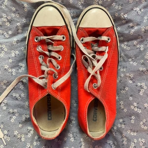 Röda Converse All Star sneakers - Säljer ett par klassiska röda Converse All Star sneakers i storlek 39. Skorna har vit gummitå, vita sömmar och grå snörning. Ovandelen är i textil och sulan i gummi. Perfekta för dig som gillar en tidlös och cool stil.