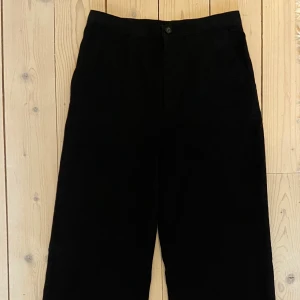 Svarta kostymbyxor från H&M - Svarta kostymbyxor från H&M med rak passform och dekorations fickor bak. Byxorna har hög midja, dragkedja och knappstängning framtill. Slitsar längs ned som ger en utsvängd look. Storlek 13-14 år men passar runt XS. 