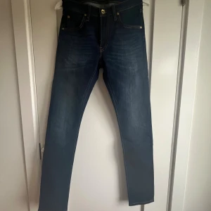 Mörkblå skinny jeans från Lee - Snygga mörkblå jeans från Lee med klassisk femficksdesign och kontrastsömmar. Jeansen har en smal passform och raka ben, tillverkade i slitstarkt denimtyg. Perfekta för dig som gillar en stilren och tidlös look.