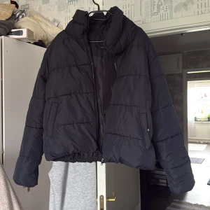 Svart pufferjacka från 157 L - Säljer en svart pufferjacka från 157 i storlek L. Jackan har hög krage, dragkedja framtill och två sidofickor. Den är quiltad och har en loose passform, perfekt för kalla dagar. Materialet är syntet och jackan är riktigt skön att bära.