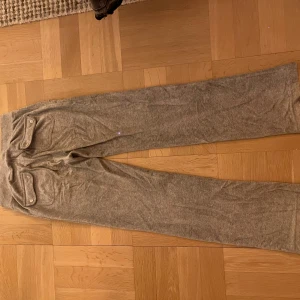 Grå juicy couture med fickor - Grå juicy couture mjukis i mjukt material med raka ben och två bakfickor med lock och knappar. Perfekta för en chill och avslappnad stil. Byxorna har en enkel design och är riktigt sköna att ha på sig.