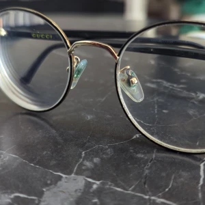 Runda glasögon från Gucci i guld - Snygga runda glasögon från Gucci med tunna guldfärgade metallbågar och svarta skalmar. Klassisk och stilren design med diskret Gucci-logga på sidan. Passar dig som vill ha en tidlös och trendig look. Länk : https://pretavoir.co.uk/products/gucci-gg0297ok-003?srsltid=AfmBOortyWlSffb_2mm9dhXJd5CGlIHLyvvpV634NK1tkDIiuh_SjCqp&utm_source=chatgpt.com&shpxid=f1b93da9-1d4c-4d0f-9a72-8eb99692adba