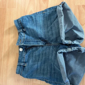 Blå jeansshorts med uppvik - Snygga blå jeansshorts med hög midja och  med klassisk femficksdesign och uppvikta benslut. De har bälteshällor, knapp och dragkedja framtill samt två bakfickor. Perfekta för en avslappnad och cool stil under varma dagar.