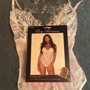 Vit spetsbody från Leg Avenue - Supersnygg vit body i transparent mesh och spets från Leg Avenue. Den har tunna axelband, v-ringad urringning och fina spetsdetaljer framtill och baktill. Söt rosett på ryggen och vackra spetskanter ger en extra touch. Perfekt för dig som vill känna dig extra fin.