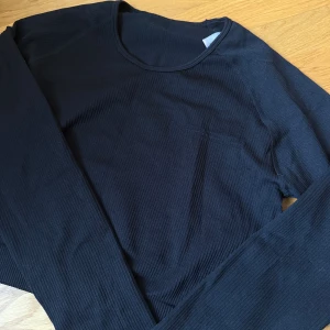 Svart ribbad långärmad tröja XL - Svart långärmad i storlek XL. Tröjan är ribbad och har en rund halsringning samt en liten bröstficka. Perfekt för dig som gillar en enkel och stilren look. Perfekt till träning. 