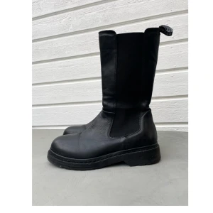 Svarta välvårdade boots från Musse&Cloud  Stl. 40 - Svarta boots i skinn från Musse&Cloud med rund tå, platt sula och dragkedja på insidan. Skaftet är högt och fodrat med ett mjukt tyg i rutigt mönster. Praktiska dragflikar upptill för enkel påtagning. Perfekta för höst och vinter. Välvårdade och sparsamt använda pga fel storlek. 