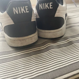 Nike Court Vision svartvita sneakers - Svartvita Nike Court Vision sneakers med klassisk design, vit sula och svarta detaljer. Skorna har snörning, rund tå och är tillverkade i syntet och skinn. Perfekta för dig som gillar en clean och sportig look.