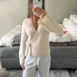 Beige omlottkofta från Gina Tricot - Supermjuk beige omlottkofta från Gina Tricot med knyt i sidan och ribbade muddar. Koftan är stickad och har lång ärm 💗