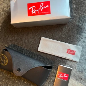 Svarta Ray-Ban Wayfarer solglasögon - Klassiska svarta Ray-Ban Wayfarer solglasögon med glansig båge och mörka linser. Ikonisk modell med Ray-Ban-logga på skalmen. Kommer med originalfodral, putsduk och box. Perfekt accessoar för en cool och tidlös stil.