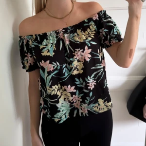 Blommig offshoulder topp  - Säljer en svart offshoulder topp från Gina Tricot med blommigt mönster i pastelliga färger som ljusgul, rosa och mintgrön. Storlek M passar S 