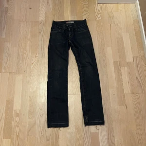 Levi's 511 mörkblå jeans - Mörkblå Levi's 511 jeans med klassisk femficksdesign och raka ben. Jeansen har en snygg tvätt och subtila slitningar vid benslut. Tillverkade i robust denim med Levi's ikoniska läderpatch bak i midjan och röda logotag på bakfickan.