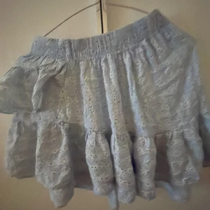 Ljusblå volangkjol från ONLY - Supersöt ljusblå kortkjol från ONLY med broderade hål och volangdetaljer. Kjolen har resår i midjan och en romantisk känsla med sin spets och volanger. Perfekt för dig som vill ha en feminin och trendig look.