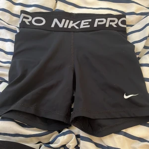 Nike Pro Dri-FIT svarta träningstights - Svarta Nike Pro Dri-FIT shorts med bred resår i midjan där det står NIKE PRO i vitt. Tight passform och tillverkade i ett stretchigt, snabbtorkande syntetmaterial. Perfekta för träning och sport. Klassisk Nike Swoosh-logga på benet.