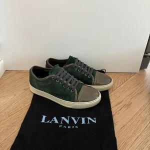 Gröna lanvins - Snygga gröna sneakers från Lanvin med ovandel i mocka och lackad tå i olivgrönt. Skorna har grå snörning och vit sula med Lanvin-logga undertill. Perfekt för dig som vill ha en unik och lyxig touch på din outfit. Använda några gånger men är k riktigt bra skick! Dustbag tillkommer:) skorna är i UK 5 vilket motsvarar 39-40 men sitter som 41 men går att ha som 39 också!