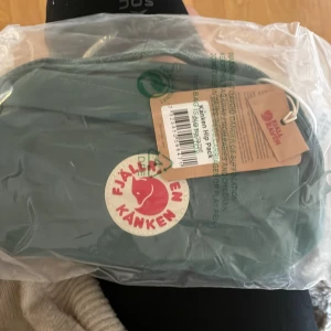 Grön Kånken Hip Pack från Fjällräven - Snygg grön Kånken Hip Pack från Fjällräven med klassisk rund logga framtill. Praktisk midjeväska i slitstarkt material med dragkedja och justerbart band. Perfekt för att bära det viktigaste när du är på språng.aldrig använd