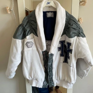 Vit och grå bomberjacka från Zero 5 - Säljer en Unik  vit bomberjacka  från År 1998 . Mycket skön varm . Jackan har stora bokstäver framtill, ribbade muddar och knappar. Oversized passform och sportig collegekänsla. Perfekt för dig som gillar streetwear.säg om ni vill exat mått