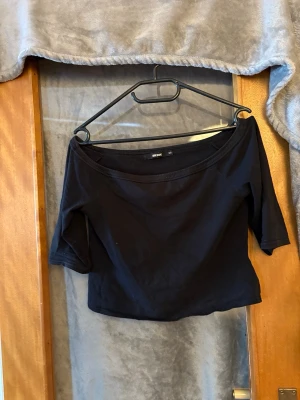 Svart offshoulder topp från Bik Bok - Trendig svart offshoulder topp från Bik Bok med croppad passform. Toppen är ärmlös över axlarna och har en enkel, stilren design i mjukt bomullsmaterial. Perfekt att matcha med höga jeans eller kjol för en snygg look.