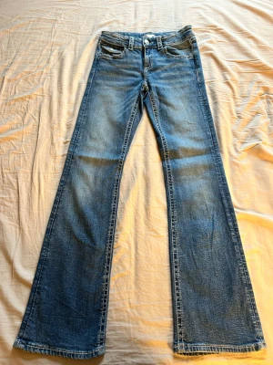 Blå bootcut jeans från Gina Tricot - Snygga blå bootcut jeans från Gina Tricot i klassisk denim med fem fickor och normal midja. Jeansen har en lätt tvättad look och vida ben som ger en retrovibe. Perfekta att styla med sneakers eller boots.