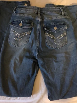 Blå jeans med broderade bakfickor - Säljer ett par blå jeans från shein med snygga broderade detaljer på bakfickorna och lock med knapp. Andvänt få gånger och inga tecken på slitningar. 