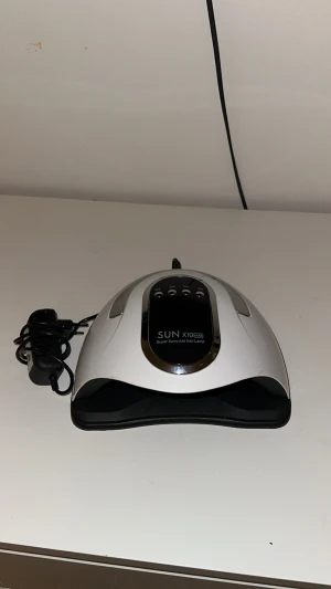 SUN X10 Max UV LED nagellampa - UV LED nagellampa från SUN, modell X10 Max. Lampan är vit och svart med digital display och flera timerinställningar. Perfekt för att härda gelélack och andra nagelprodukter. Utrustad med många LED-lampor för jämn belysning och snabb torkning.