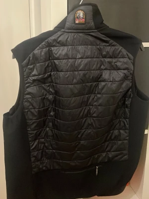 Svart dunväst från Parajumpers - Stilren svart dunväst från Parajumpers med quiltat mönster och hög krage. Västen har dragkedja framtill, bröstficka med dragkedja och klassisk logotyp vid nacken. Perfekt för lager-på-lager och håller dig varm under kyliga dagar. Pris kan diskuteras 